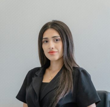 A woman in a black suit sits in a chair.
